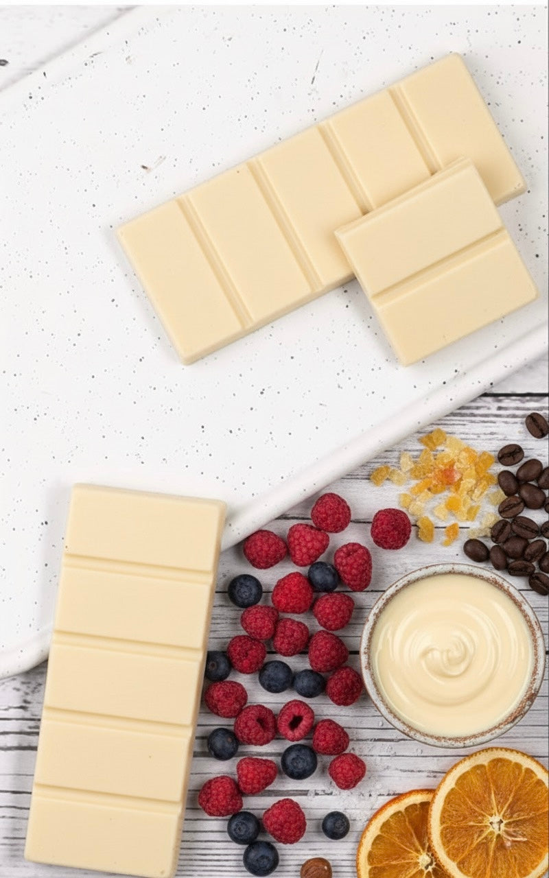 White chocolate bars with berries, coffee beans, and a bowl of cream on a white surface.